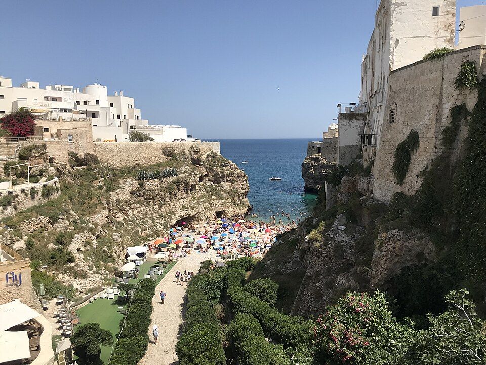 Pláž Polignano a Mare v létě 2023 — oblázková zátoka s koupajícími se lidmi